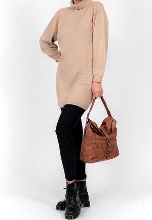 Beige gebreide jurk met een hoge kraag, lange mouwen, gecombineerd met zwarte leggings en zwarte veterschoenen. Houdt een bruine leren handtas vast.