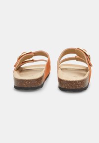 Sandali in suede arancione con base in sughero. Presentano due cinturini regolabili e una fibbia in tonalità oro. Suola piatta con un battistrada in gomma nera testurizzata.