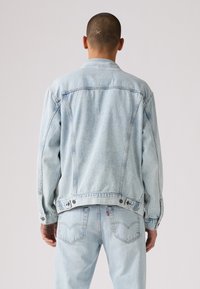 Svetlo modra jeans jakna ima sproščen dizajn, vidno šivanje, gumbne detajle in nekoliko obrabljeno teksturo na hrbtni strani.