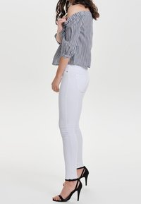 Off-the-shoulder striped blouse with puffed sleeves in navy and white, paired with white skinny jeans and black stiletto heels.