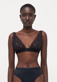 Bralette in pizzo nero con un design a scollo a V profondo e spalline larghe, motivo floreale e una texture morbida. Abbinato a un bottom nero a vita alta.