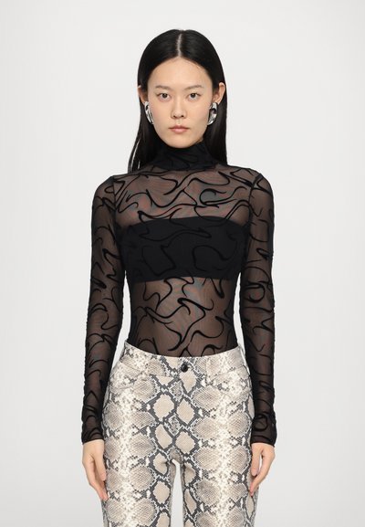 Haut à manches longues en mesh noir avec un motif abstrait de tourbillon noir sur un panneau uni. Associé à un pantalon imitant le motif serpent beige et gris.