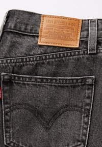 Los pantalones de mezclilla negros de Levi's cuentan con un parche de cuero marrón con una marca embellecida y un diseño clásico de costura en forma de V en el bolsillo trasero.