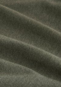 Olivenfarbener Stoff mit einer weichen, strukturierten Oberfläche, die dezente Variationen in Webart und Farbnuance aufweist, angeordnet in einer drapierten, geschichteten Weise.