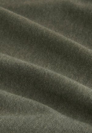 Oliwkowa tkanina o miękkiej, teksturowanej powierzchni, z subtelnymi wariacjami w splocie i tonacji, ułożona w sposób zwisający i warstwowy.