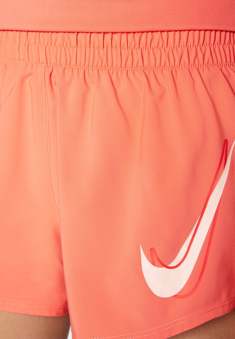 Pantalones cortos deportivos de color coral con una cintura elástica, textura suave y un destacado logo en forma de swoosh blanco en el costado.