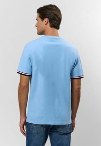 Svetlomodré tričko s krátkym rukávom a okrúhlym výstrihom. Obsahuje pruhované čierne, červené a biele akcenty na okrajoch rukávov. Mäkký bavlnený materiál.