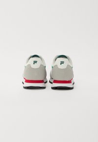 Hvit og grå sneakers med tealdetaljer, med en sølvfarget teksturert hæl, rød mellomsåle og svart gummisåle. F-logo på hælen.