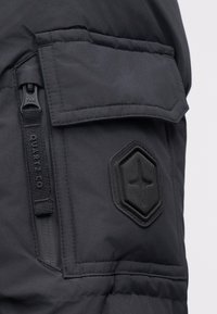 Μαύρο επενδεδυμένο μπουφάν με υφή, εξαγωνική θήκη και τσέπη με φερμουάρ. Διαθέτει φερμουάρ YKK και ενισχυμένες ραφές για αυξημένη ανθεκτικότητα.