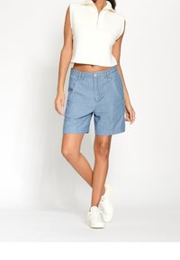 Světle modré šortky z chambray s přiléhavým střihem, předními kapsami a zapínáním na knoflík. V kombinaci s bílým topem bez rukávů s rib strukturovaným vzorem a bílými teniskami.