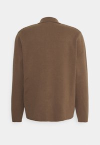 Chemise marron à manches longues avec boutons, de texture douce, dotée d'un col classique et d'un design uni sans attaches apparentes ni motifs.