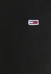 Tessuto a coste nero con un piccolo logo ricamato in rosso, bianco e blu. Il design enfatizza la texture e i dettagli del marchio in modo sottile.