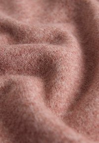 Miękka różowa wełna o gładkiej, lekko teksturowanej powierzchni, z subtelnym wzorem melanżowym. Łagodne układanie tworzy płynne krzywe.