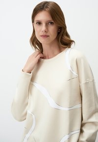 Lichtbeige sweatshirt van zacht materiaal, met abstracte witte en zilveren lijnen. Ronde halslijn en een ontspannen pasvorm met lange mouwen.