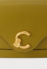 Olijfgroene leren tasklep met zichtbare stiksels en een glanzende gouden metalen gesp in de vorm van een gestileerde letter C.