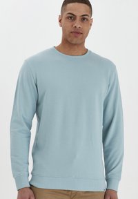 Lichtblauwe longsleeve sweatshirt gemaakt van zacht materiaal. Heeft een ronde hals, ribgebreide manchetten en een rechte zoom. Eenvoudig ontwerp, zonder patronen.