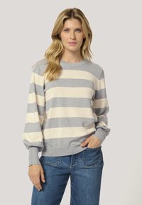 Sweter w paski w odcieniach szarości i kremu, z okrągłym dekoltem, balonowymi rękawami i prążkowanymi mankietami, zestawiony z niebieskimi dżinsami.