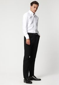 Biała koszula z długim rękawem i kołnierzykiem zapinanym na guziki, w zestawieniu z dopasowanymi czarnymi spodniami i czarnymi butami wizytowymi. Prosty, dobrze dopasowany krój.