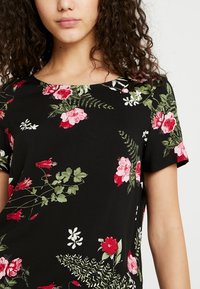 Top negro de flores con escote redondo, mangas cortas y un vibrante patrón de flores rojas y blancas con hojas verdes.