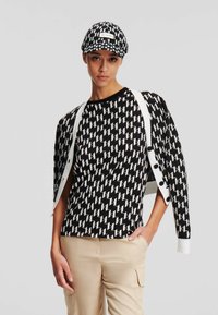 Maglione a maglia in bianco e nero con motivo, accompagnato da un berretto coordinato, dotato di scollo rotondo e dettagli con bottoni, abbinato a pantaloni cargo beige.