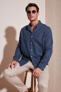 Camicia button-up blu navy realizzata in tessuto testurizzato, maniche lunghe e vestibilità rilassata, abbinata a pantaloni beige e occhiali da sole rotondi.