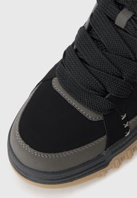 Black and gray sneaker featuring a textured upper and thick laces, with a contrasting rubber outsole and visible stitching details.