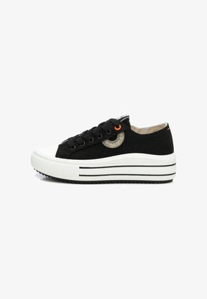 Zapatillas de lona negras con una puntera y suela de goma blanca, que presentan un acento naranja y un detalle de diseño circular en el lateral.
