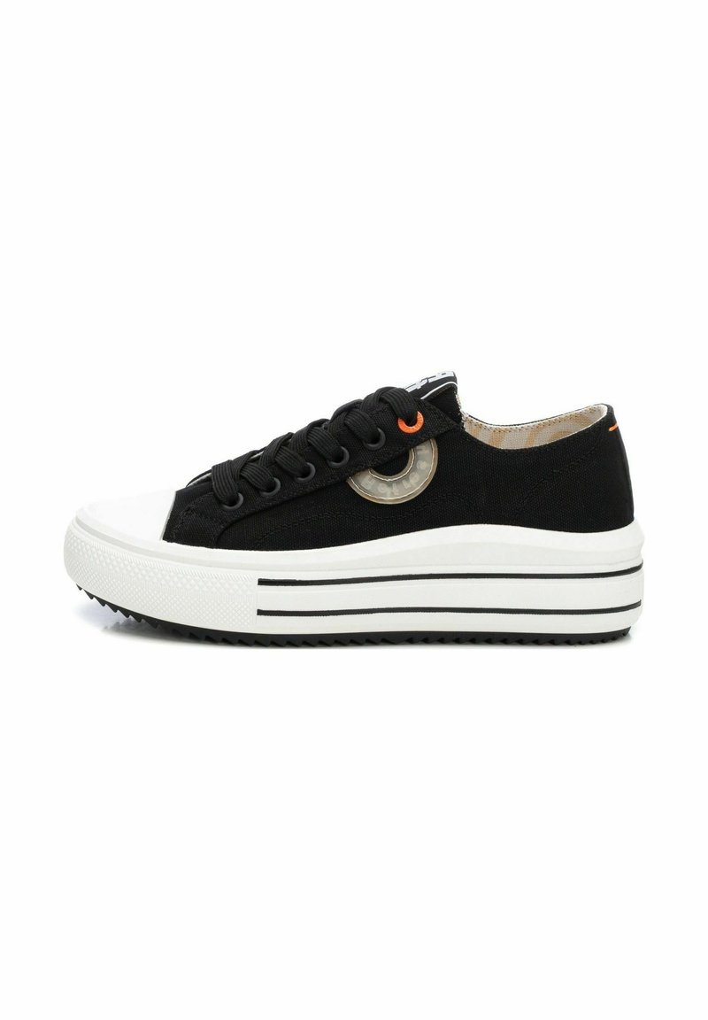 Zapatillas de lona negras con una puntera y suela de goma blanca, que presentan un acento naranja y un detalle de diseño circular en el lateral.