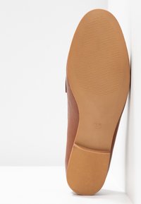 Semelle d’une chaussure en cuir marron avec des zones antidérapantes texturées et la taille 37 embossée sur la semelle en caoutchouc beige.