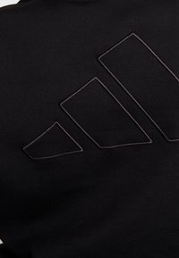 Sweat-shirt noir avec un logo brodé sombre texturé en formes géométriques dans le dos. Tissu doux avec une texture lisse.