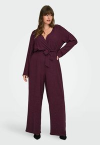 Diep bordeauxkleurige jumpsuit met een wikkelontwerp, lange mouwen, een strik in de taille en subtiele sprankelende accenten. Wijde benen en een zachte stofstructuur.