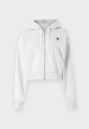 Sudadera corta gris hecha de una tela suave, que cuenta con una cremallera frontal, cordones blancos y un parche circular con el logo en el lado izquierdo del pecho.