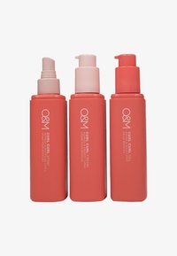 Three coral-colored bottles with pump tops, labeled as curl spray, cream, and gel. Smooth texture and sleek design for hair products.
