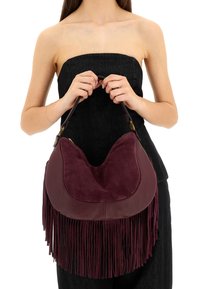 Borsa bordeaux con una combinazione di pelle liscia e scamosciata, caratterizzata da lunghe frange e una forma arrotondata, tenuta da un modello.