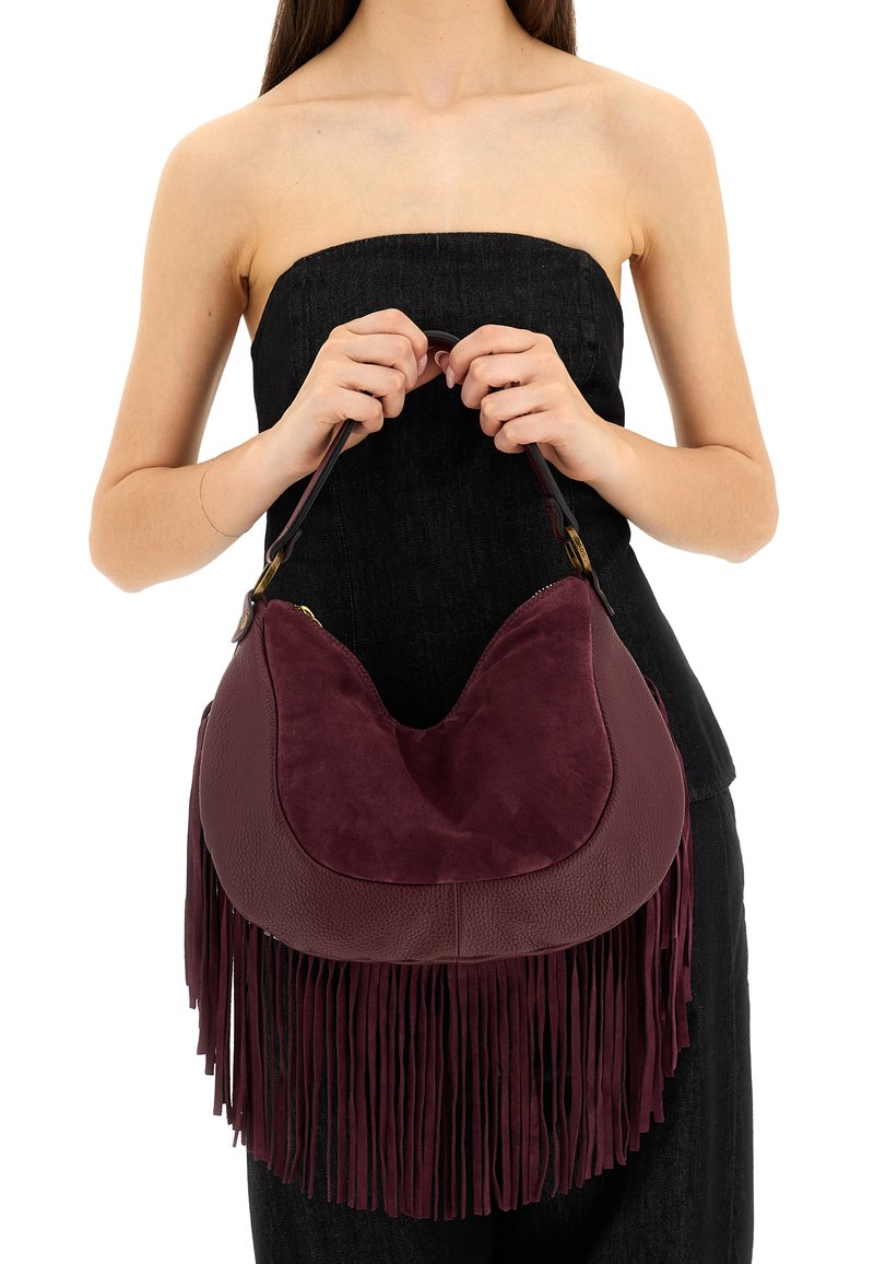Borsa bordeaux con una combinazione di pelle liscia e scamosciata, caratterizzata da lunghe frange e una forma arrotondata, tenuta da un modello.