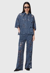 Set in pizzo a due pezzi in blu scuro, composto da una camicia a maniche corte e pantaloni a gamba larga con intricati ritagli floreali e orlo ondulato.