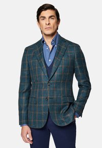 Skrzynkowy blezer w odcieniu turkusowym w kratkę, wykonany z teksturowanej tkaniny z brązowymi akcentami, zestawiony z niebieską koszulą i ciemnym kamizelka. Posiada dwie przednie kieszenie i guziki.