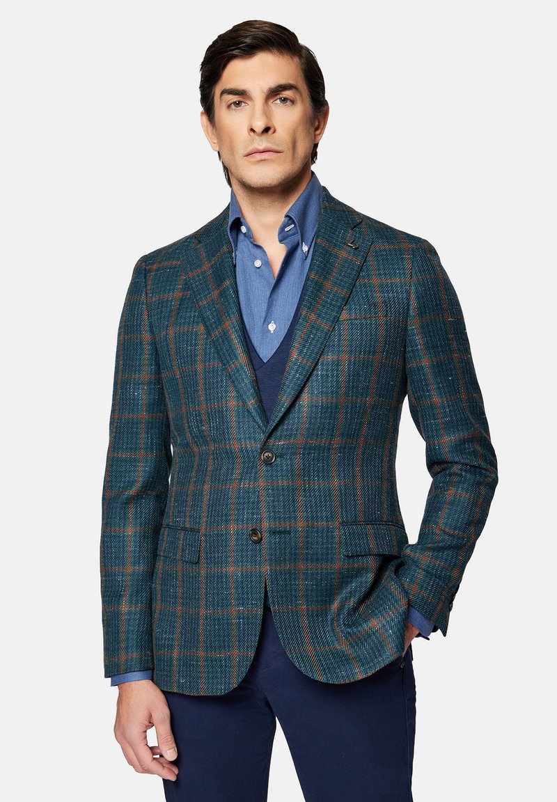 Skrzynkowy blezer w odcieniu turkusowym w kratkę, wykonany z teksturowanej tkaniny z brązowymi akcentami, zestawiony z niebieską koszulą i ciemnym kamizelka. Posiada dwie przednie kieszenie i guziki.