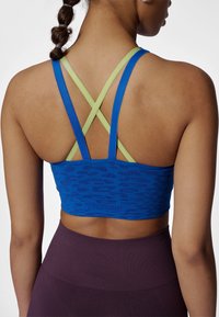 Blå sport-bh med gröna korsade band bak, med ett strukturerat mönster. Matchas med högmidjade burgundyfärgade leggings.