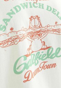 Hvid bomulds t-shirt med et tegneserie-kat, der holder en stor sandwich i orange og grøn grafik, med teksten "Galfield Downtown".