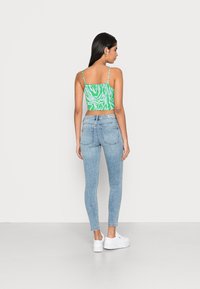 Top cropped padrão verde e branco com alças finas, combinado com jeans skinny azul claro e ténis plataformas brancos. Vista traseira.