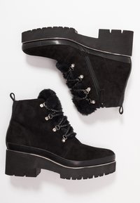 Stivaletti neri in suede con suola in gomma texturizzata, dotati di rifiniture in pelliccia sintetica, lacci decorativi e dettagli in metallo argentato.