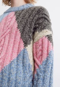 Stickad tröja med ett lapptäckesdesign i rosa, blått, grått och krämfärg. Texturerade kabelstickningar och ribbade detaljer ökar det visuella intresset.