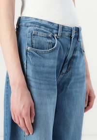 Fatos de ganga de cintura alta em azul desbotado, com um corte descontraído, grandes bolsos e aros prateados na cintura.