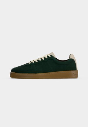 Basket en daim vert foncé à tige basse avec talon beige et lacets blancs, dotée d'une semelle en caoutchouc marron.