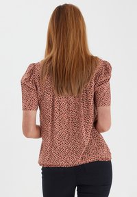Blouse à manches courtes en tissu rose, présentant un motif à pois noirs et crème, avec un détail froncé aux épaules et une coupe décontractée.