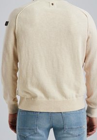 Lichtbeige gebreide trui met lange mouwen, geribbelde manchetten en zoom. Voorzien van een klein logoplaatje op de linker schouder, effen textuur.