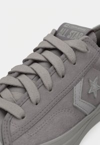 Gray suede sneaker with flat gray laces, accent star logo, and a textured upper. Features a rubber sole and stitched detailing.
