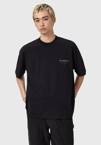 Zwarte katoenen t-shirt met ronde hals en korte mouwen, voorzien van een klein wit geborduurd logo op de borst. Soepele textuur.