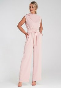 Różowy kombinezon z szerokimi nogawkami, bez rękawów, z marszczoną talią i szczegółem w postaci wiązania, wykonany z gładkiego, lekkiego materiału.